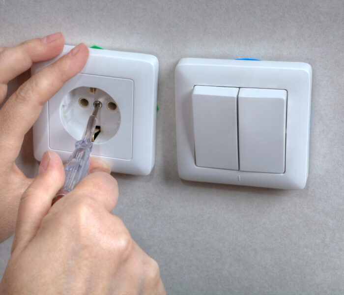 Electrician hands installing electrical wall sockets, and light switch, close-up.
